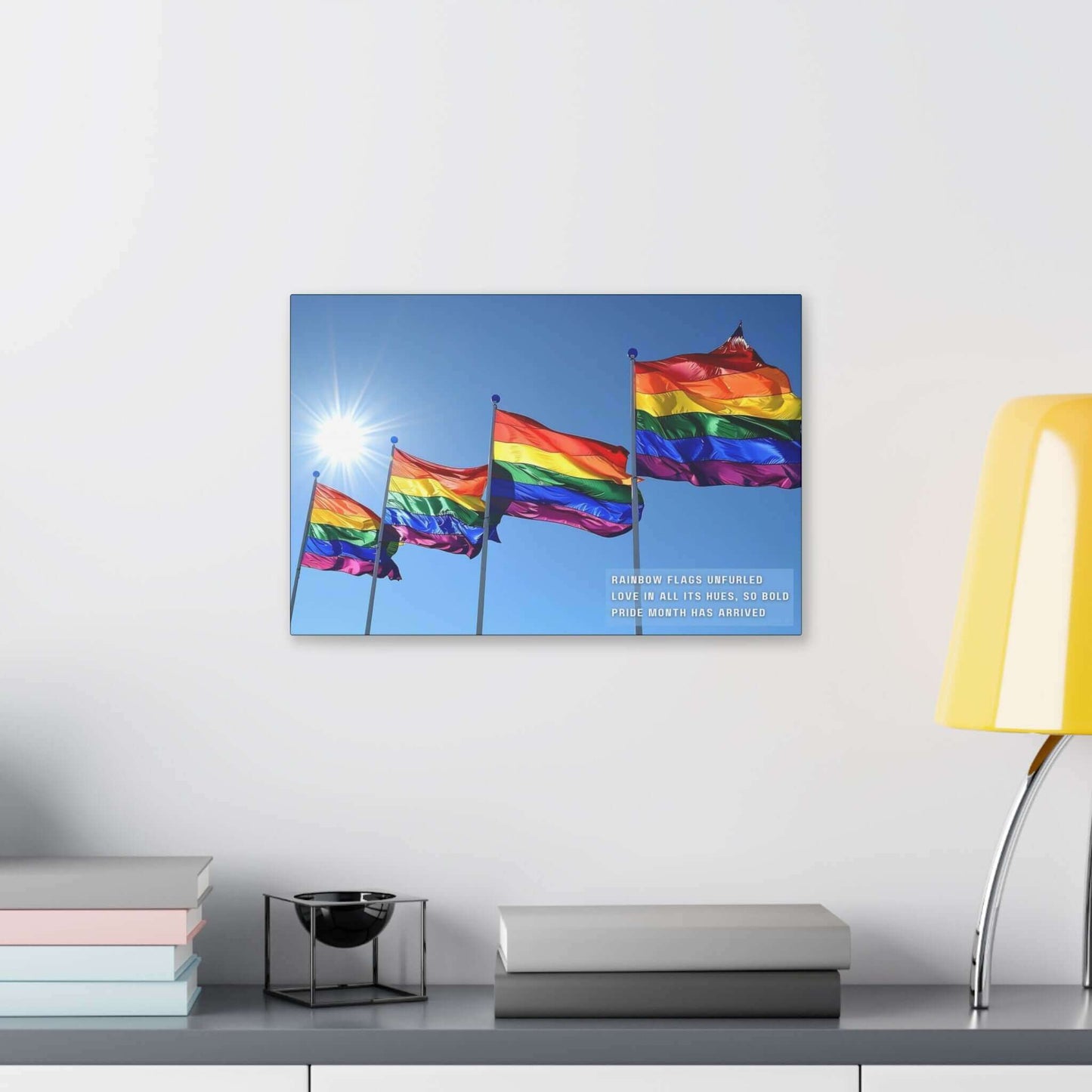 A collection of Bold Rainbow Flags Canvas Wall Art from Printify is shown flying in the breeze against a clear blue sky, with sunlight shining brightly in the background. The text on the vibrant Pride Month Art Print reads, "RAINBOW FLAGS UNFURLED LOVE IN ALL ITS HUES, SO BOLD PRIDE MONTH HAS ARRIVED," celebrating the LGBTQ+ community.