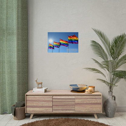 Four **Bold Rainbow Flags Poster Wall Art** wave in the breeze under a clear blue sky with the sun shining brightly. The text overlay reads, "Rainbow flags unfurled, Love in all its hues, so bold," celebrating Pride Month for the LGBTQ+ community. Created by **Printify**, this inspired piece of decor is perfect for commemorating Pride Month.